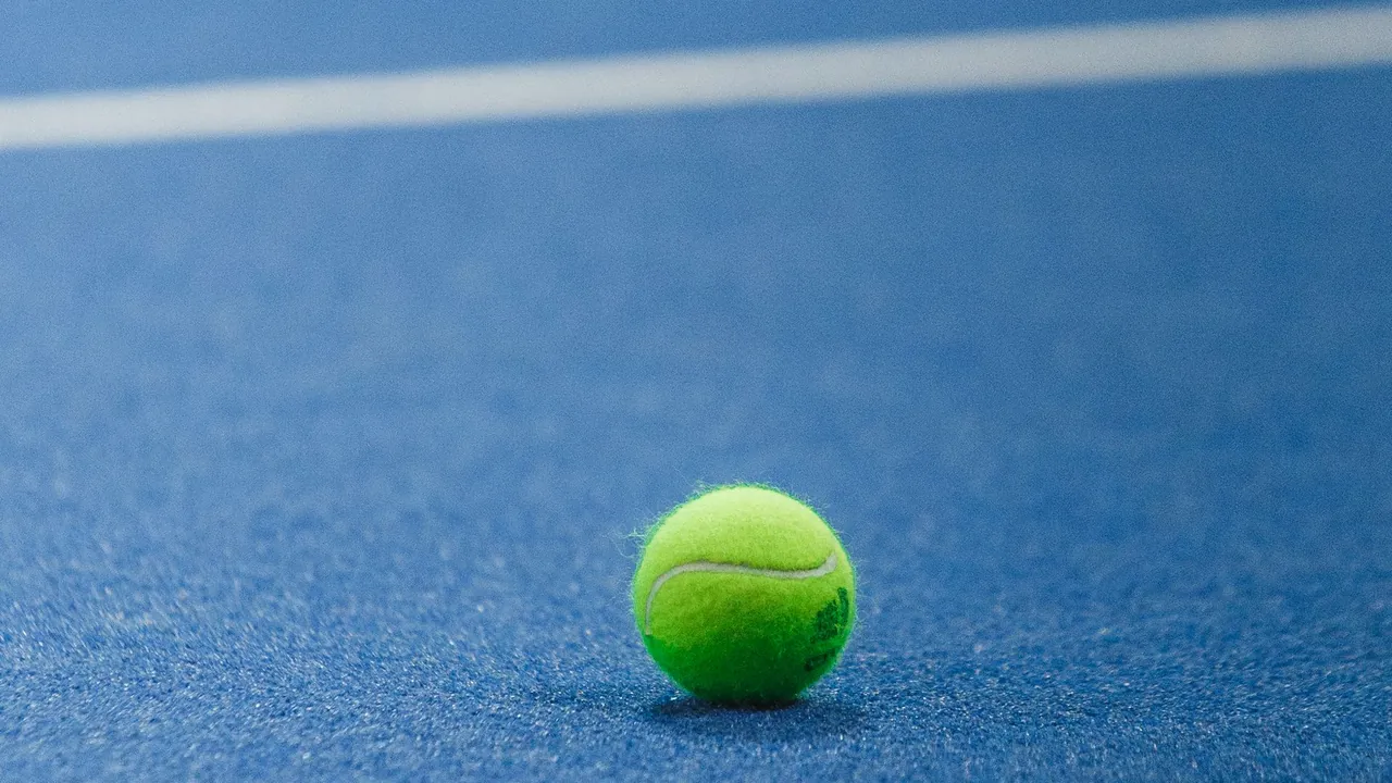 Balle de padel posée sur un gazon synthétique bleu, près d'une ligne blanche