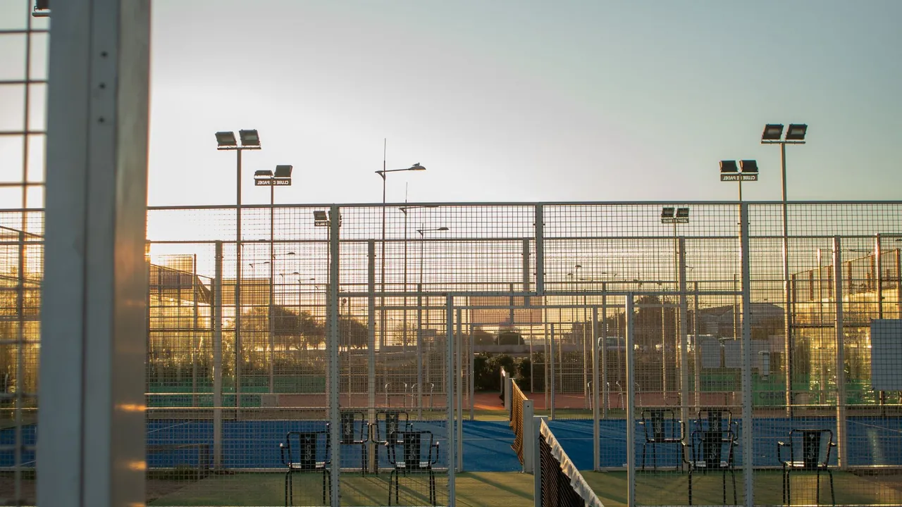 Vue d'un club de padel au coucher du soleil : grillages, courts bleus et filet